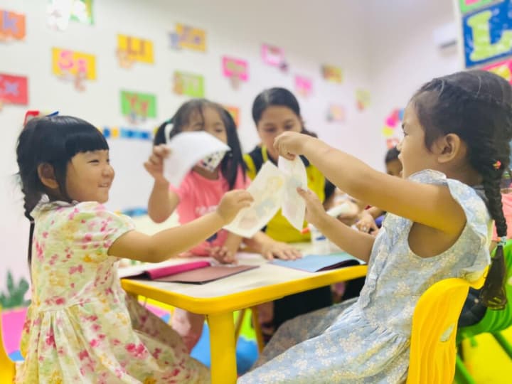カラフルな教室で、先生と一緒に工作をする幼い女の子たち